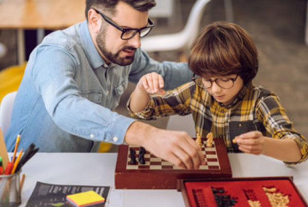 Мужчина в очках объясняет мальчику в очках, как играть в шахматы